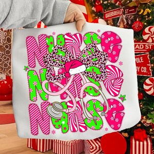 May include: White tote bag with the words "Nurse Nurse Nurse" in pink and green candy cane-style lettering. A pink stethoscope and a bow with a leopard print design and a Santa hat are featured in the design. The bag is held by a person.