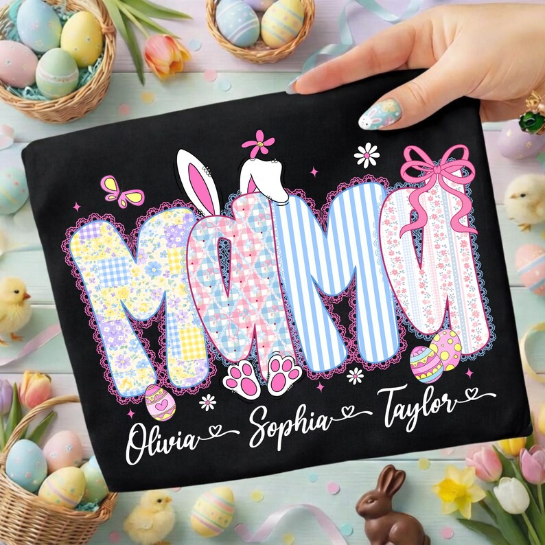 May include: Black t-shirt with the word "MOM" in a patchwork design, bunny ears, and the names Olivia, Sophia, and Taylor. The shirt has a decorative lace trim and Easter-themed accents, including eggs and butterflies.