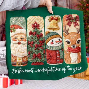 May include: A green Christmas-themed pillow featuring embroidered designs of Santa Claus, a Christmas tree, a snowman, and a reindeer. The pillow has the text "It's the most wonderful time of the year" in a white script font.
