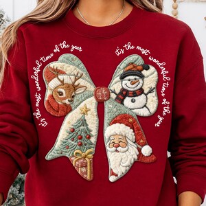 May include: A burgundy sweatshirt featuring a large bow design with Christmas-themed embroidered patches. The patches include a reindeer, snowman, Christmas tree, gift, and Santa Claus. The text "It's the most wonderful time of the year" is written around the bow.