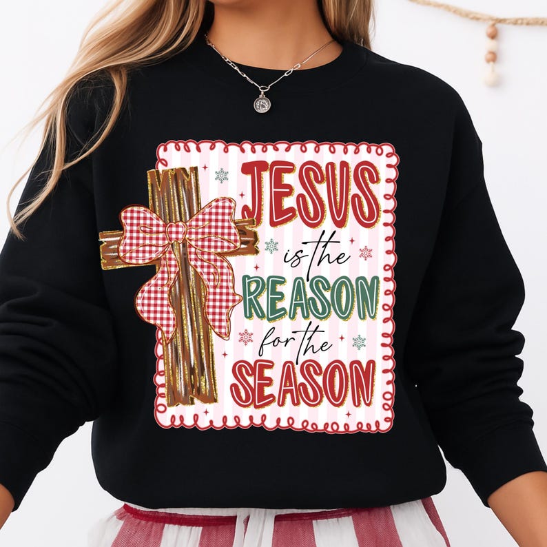 May include: Black sweatshirt featuring a decorative cross with a red and white plaid bow. The design includes the text "JESUS is the REASON for the SEASON" in red and green, with snowflake accents. A festive holiday-themed apparel item.