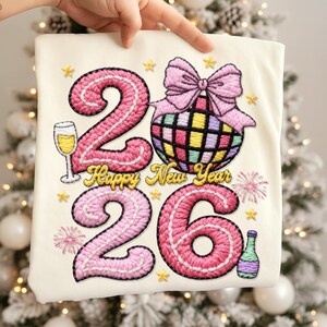May include: Off-white fabric with an embroidered design for the New Year. The design features the numbers "2026" in pink, a disco ball, champagne glass, and the text "Happy New Year". Gold stars and fireworks complete the festive look.