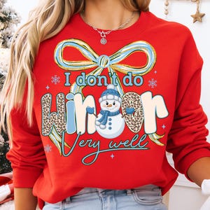 May include: Red sweatshirt with the text "I don't do winter very well." The design includes a snowman, snowflakes, and a bow. The word "winter" has a leopard print pattern.