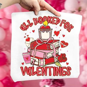 May include: White tote bag with a Valentine's Day design. The design includes a stack of books, a candle, a rose, and the text "ALL BOOKED FOR VALENTINES" in red. Pink hearts and a coffee cup are also featured.