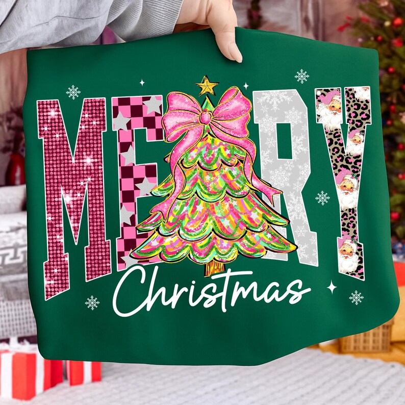 May include: A green Christmas-themed sweatshirt with the words "MERRY Christmas" in a festive design. The "M" is pink with glitter, the "E" is checkered, the "R" is white with snowflakes, and the "Y" has Santa faces. A colorful Christmas tree with a pink bow is in the center.