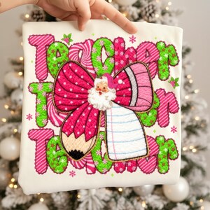 May include: Off-white fabric with the words "Teacher Team" in pink and green, featuring a Santa Claus bow and pencil design. The bow is pink with white polka dots. The pencil is brown and pink. The background is a Christmas tree.