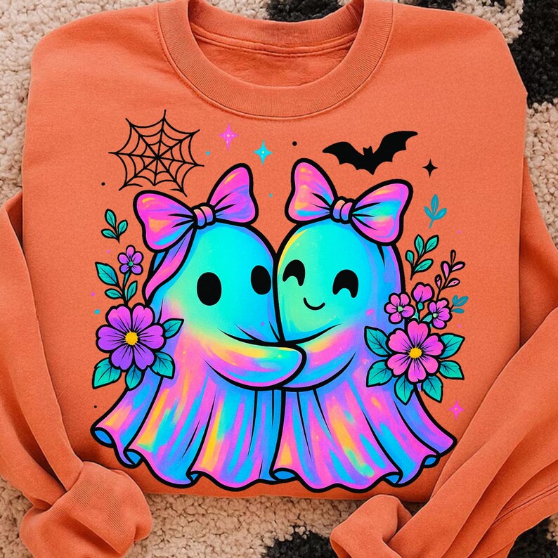 May include: Orange sweatshirt featuring a colorful graphic of two hugging ghosts with bows, surrounded by flowers, a spiderweb, and a bat. The ghosts have a rainbow-like appearance. A cute and friendly design.