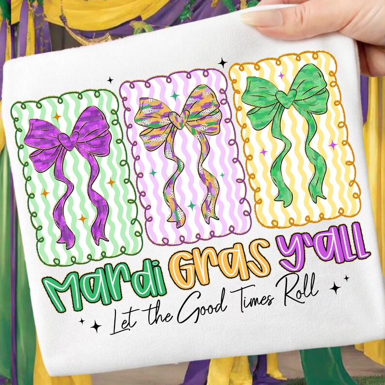 May include: White Mardi Gras themed towel featuring three colorful bows in purple, green, and gold. The text "Mardi Gras y'all" and "Let the Good Times Roll" are printed below the bows. The towel is held by a hand.