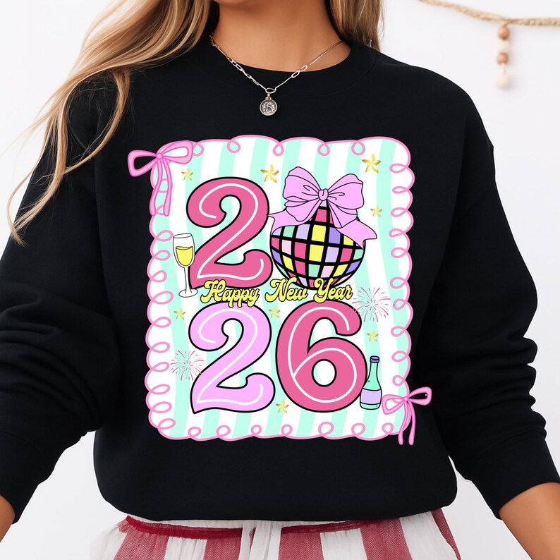 May include: Black sweatshirt with a colorful graphic design for the New Year. The design includes the numbers "26" in pink, a disco ball, champagne, and the text "Happy New Year". The design is framed with a pink border and bows.