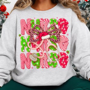 May include: A light gray sweatshirt featuring a festive design for nurses. The word "NURSE" is spelled out in green and pink candy cane-style letters. A pink stethoscope and a bow with a Santa hat complete the holiday theme.