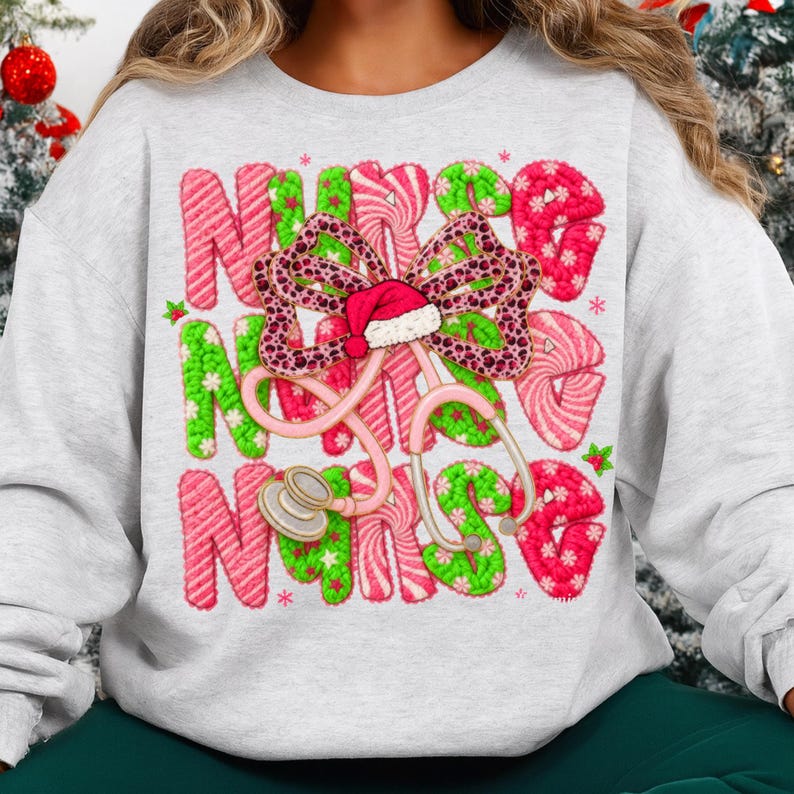 May include: A light gray sweatshirt featuring a festive design for nurses. The word "NURSE" is spelled out in green and pink candy cane-style letters. A pink stethoscope and a bow with a Santa hat complete the holiday theme.