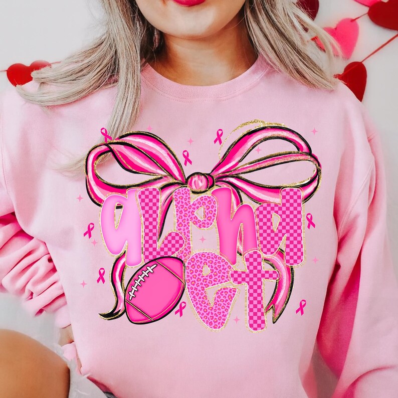 May include: Pink sweatshirt with a large bow and the words "Alright Get" in pink and gold lettering. A pink football and pink ribbons are also featured on the sweatshirt. The sweatshirt is a solid pink color.
