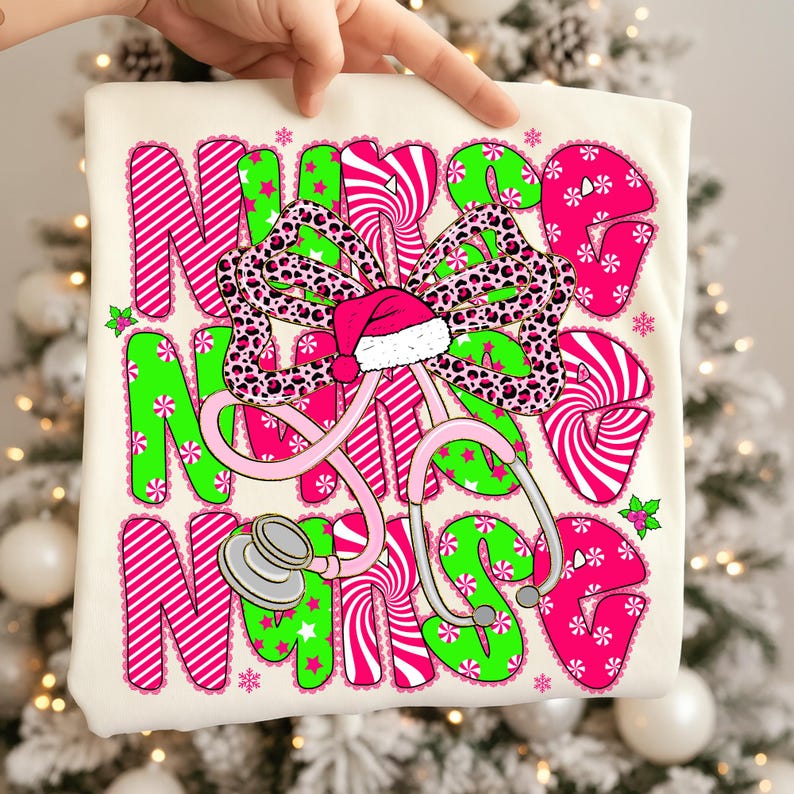 May include: A cream-colored t-shirt with a festive design. The words "NURSE" are displayed in pink and green, with a bow and Santa hat. A pink stethoscope is also featured. The design includes snowflakes and candy cane stripes.