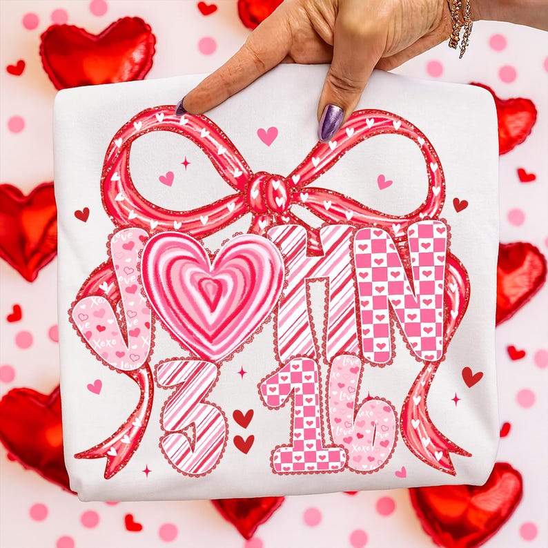 May include: White t-shirt featuring a large red bow with a heart-shaped design. The shirt has the text "JOIN 3 16" in a mix of pink and red patterns, including hearts and stripes. Small red hearts are scattered around the design.