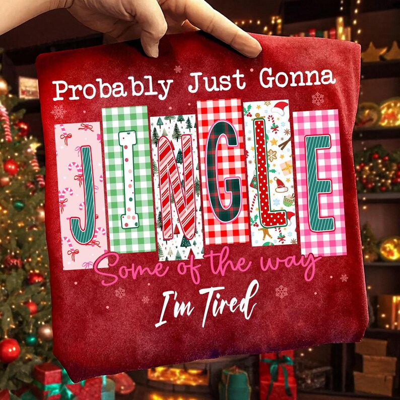 May include: A red Christmas-themed shirt with the words "Probably Just Gonna Jingle Some of the way I'm Tired" in white and pink. The word "JINGLE" is in a variety of festive patterns and colors, including green, red, and pink.