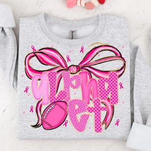May include: A light gray sweatshirt with a large pink bow and the words "Alpha Get" in pink. The letters have a mix of leopard print and checkered patterns. A pink football and pink ribbons are also featured.