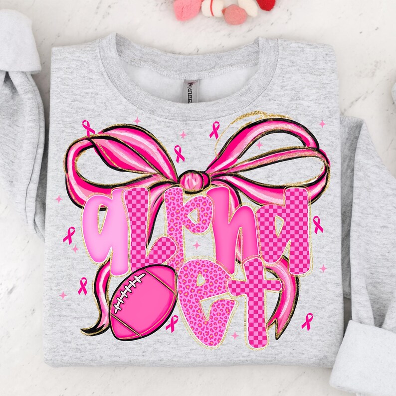 May include: A light gray sweatshirt with a large pink bow and the words "Alpha Get" in pink. The letters have a mix of leopard print and checkered patterns. A pink football and pink ribbons are also featured.