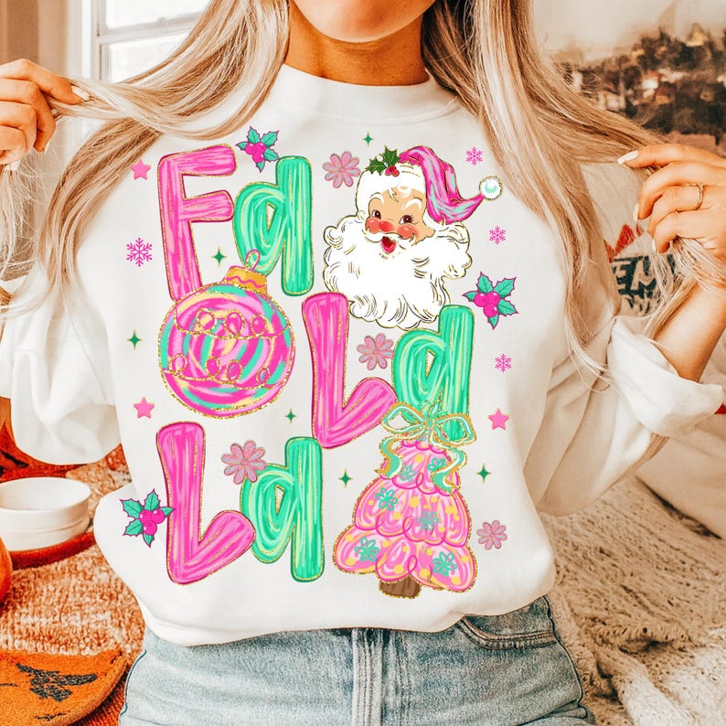 May include: White sweatshirt with the words "Fa La La La La" in pink and green, along with a Santa Claus graphic and Christmas tree design. The sweatshirt has a festive holiday theme.
