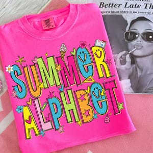 May include: A vibrant pink t-shirt featuring the words "SUMMER ALPHABET" in a fun, colourful font. The design incorporates stars, flowers, and an ice cream cone. The t-shirt is made of a soft fabric.