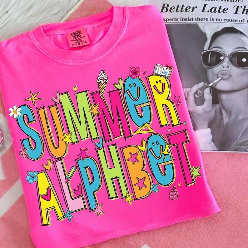 May include: A vibrant pink t-shirt featuring the words "SUMMER ALPHABET" in a fun, colourful font. The design incorporates stars, flowers, and an ice cream cone. The t-shirt is made of a soft fabric.