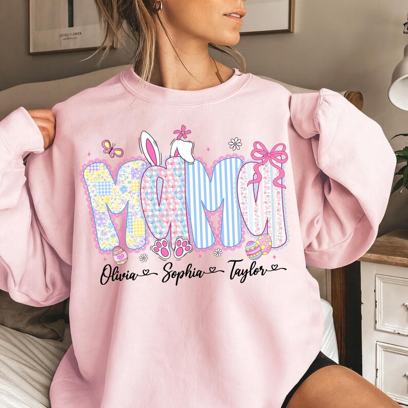 May include: A light pink sweatshirt with the word "MAMA" in a patchwork design, blue stripes, and a pink bow. Easter-themed graphics include bunny ears, eggs, and paw prints. The names Olivia, Sophia, and Taylor are below.