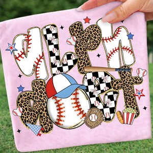 May include: Pink t-shirt with the words "MLB Mom" in a baseball-themed design. The letters have baseball stitching, leopard print, and checkered patterns. A baseball, glove, and hat are also featured.
