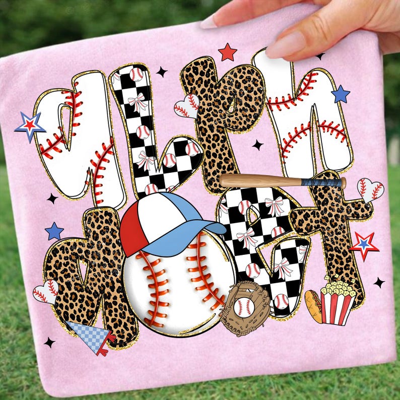 May include: Pink t-shirt with the words "MLB Mom" in a baseball-themed design. The letters have baseball stitching, leopard print, and checkered patterns. A baseball, glove, and hat are also featured.