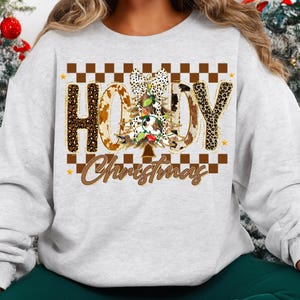 May include: A light gray sweatshirt with a festive design. The word "HOODY" is spelled out in a mix of leopard and cow print. A Christmas tree is in the center, and the word "Christmas" is written below.