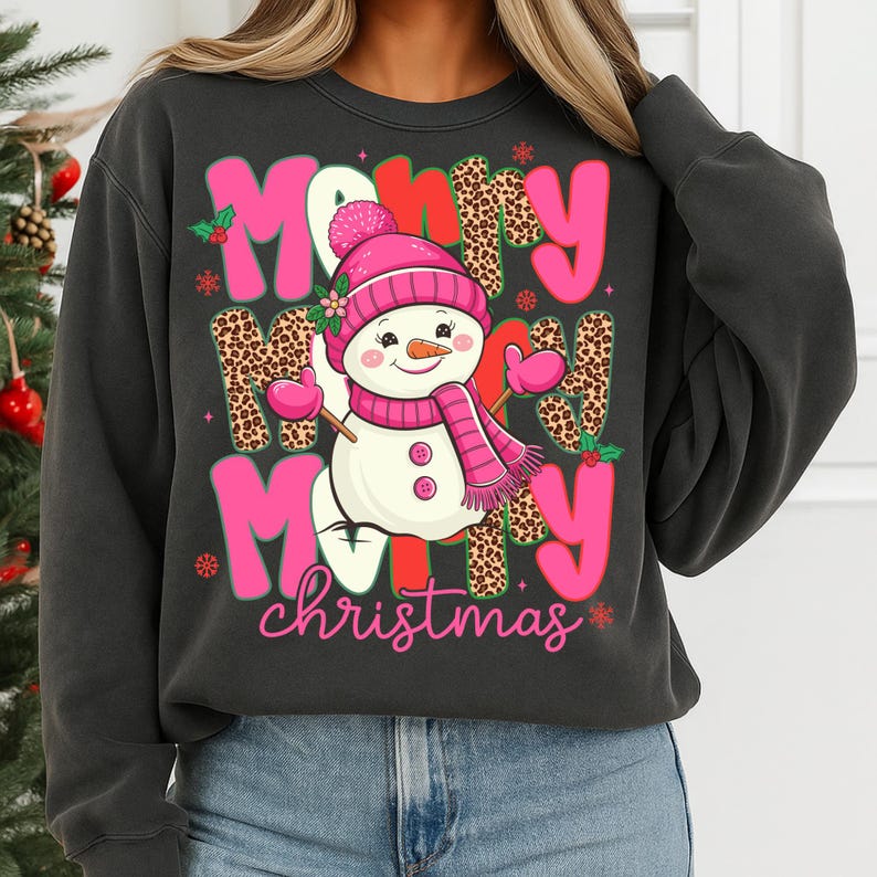 May include: Dark gray sweatshirt with a festive Christmas design. The design features the words "Merry Christmas" in pink and red, with a snowman wearing a pink hat and scarf. The letters have a leopard print pattern.