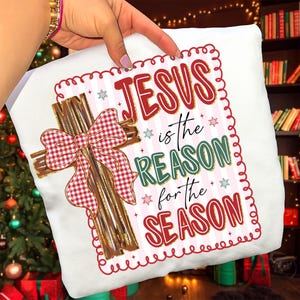 May include: White pillow with a Christmas theme. The pillow features a cross made of wooden slats with a red and white checkered bow. The text "JESUS is the REASON for the SEASON" is printed on the pillow in red and green.