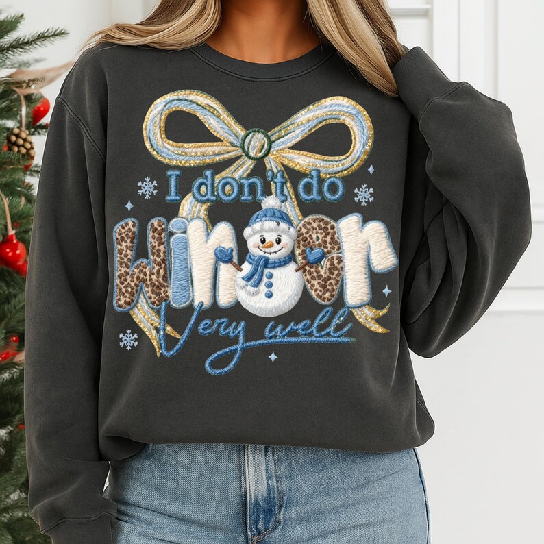 May include: Dark gray sweatshirt with a whimsical winter design. The graphic features a snowman wearing a blue hat and scarf, with the text "I don't do winter very well." The word "winter" has a leopard print pattern. A large bow is at the top.