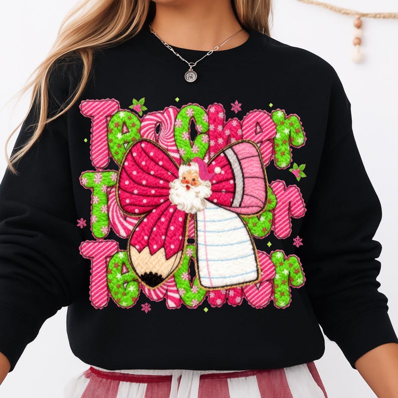 May include: Black sweatshirt with a colorful graphic design. The design features the word "Teacher" in pink and green, a pink bow, a pencil, and a Santa Claus figure. The sweatshirt is a festive holiday item.