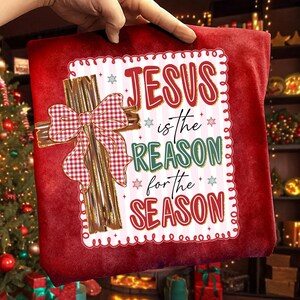 May include: Red Christmas pillow with the text "JESUS is the REASON for the SEASON". The pillow features a gold cross with a red and white plaid bow. Snowflakes and decorative border complete the design.