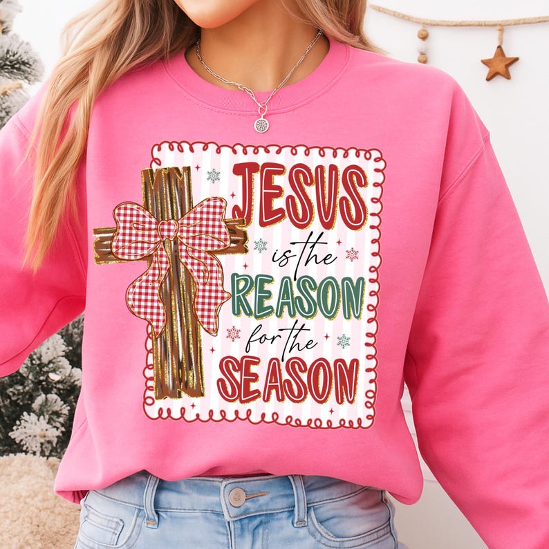 May include: Pink sweatshirt with the text "JESUS is the REASON for the SEASON" in red and green. A cross with a plaid bow is on the left side of the text. The sweatshirt is a crew neck style.