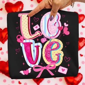 以下が含まれることがあります： カラフルで気まぐれなデザインの「LOVE」という文字がプリントされた黒いTシャツ。文字はハート、ストライプ、花柄で装飾されています。ピンクのリボンとハート型の風船がロマンチックなテーマを盛り上げています。デザインには南京錠、封筒、翼のあるハートが含まれています。