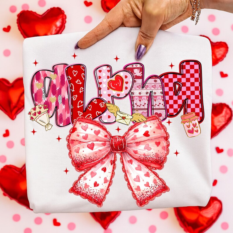 May include: White sweatshirt with the word "ALHAM" in a colorful, Valentine's Day-themed design. The letters feature hearts, patterns, and a large red bow with heart details. The background includes red heart-shaped balloons.