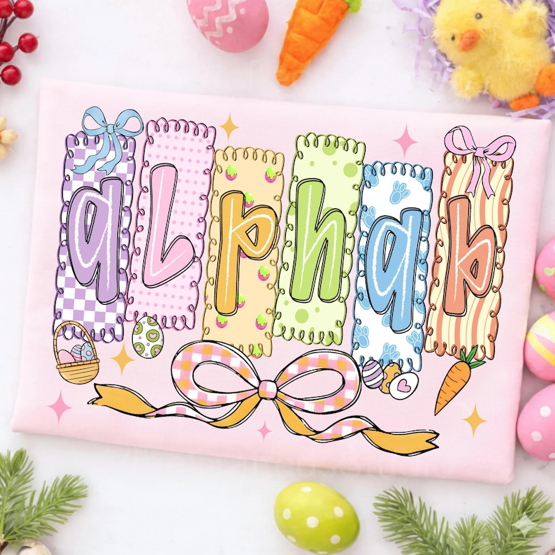 May include: A pink Easter-themed shirt with the word "alphabet" in colorful, decorative letters. Each letter is in a different color and pattern, with Easter eggs, bows, and carrots. The design is whimsical and festive.