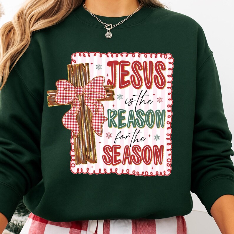 May include: Dark green sweatshirt with a decorative cross and the text "JESUS is the REASON for the SEASON" in red and green. The cross is brown with a red and white checkered bow. The text is inside a white frame with red trim.