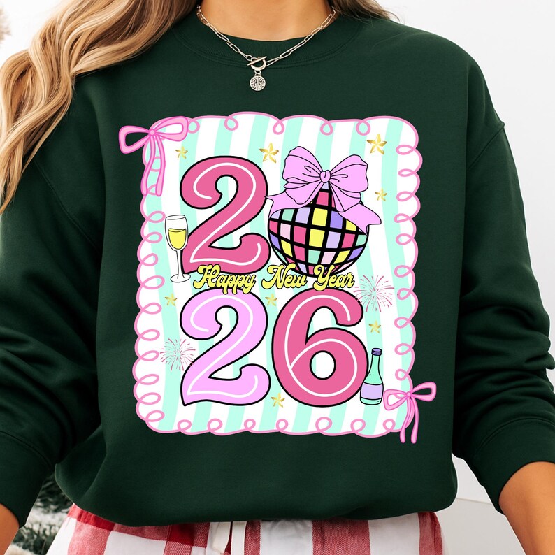 May include: Dark green sweatshirt with a colorful graphic design. The design features the numbers "26" in pink, a disco ball, a champagne glass, and the words "Happy New Year". The design is framed with a light blue and white striped background.