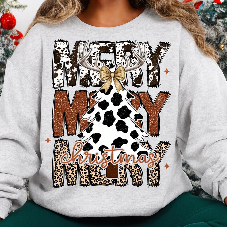 May include: A light gray sweatshirt with a Christmas tree design. The tree is white with black spots, antlers, and a gold bow. The words "MERRY CHRISTMAS" are printed in brown and leopard print.