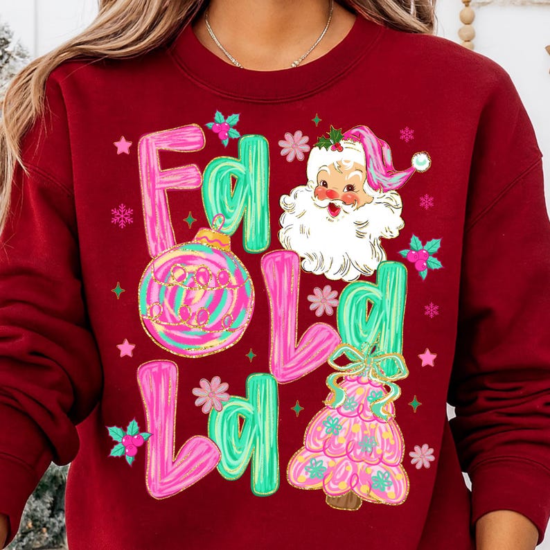 May include: A maroon sweatshirt with a festive design. The design includes the words "Fa La La" in pink and green, a Santa Claus illustration, a Christmas tree, and a decorative ornament. The design is embellished with stars and snowflakes.