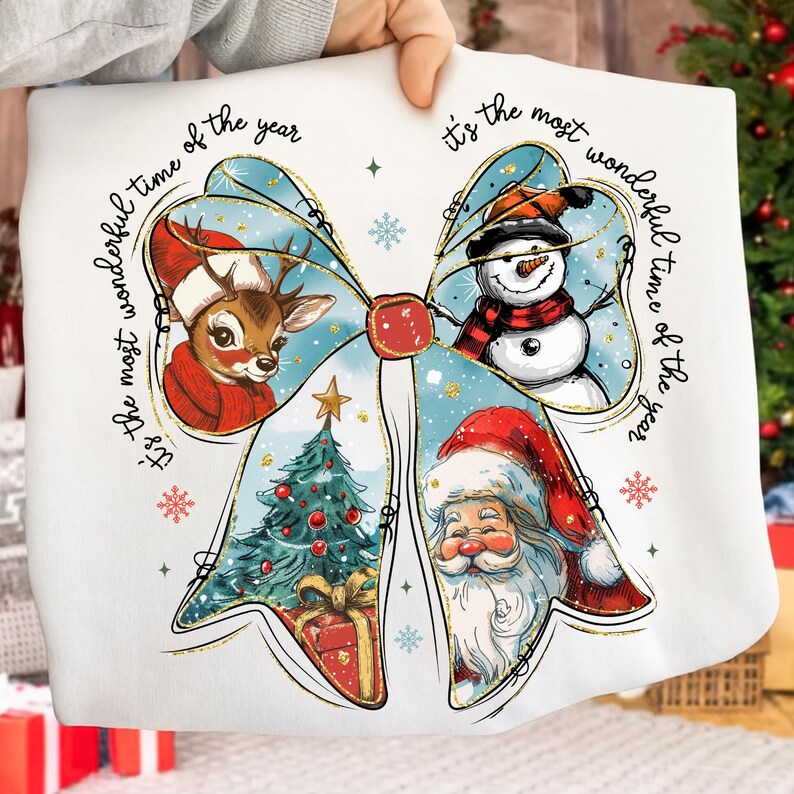 May include: White sweatshirt featuring a Christmas bow design with a reindeer, snowman, Christmas tree, and Santa Claus. The text "It's the most wonderful time of the year" is printed around the bow. The design includes snowflakes and gold accents.