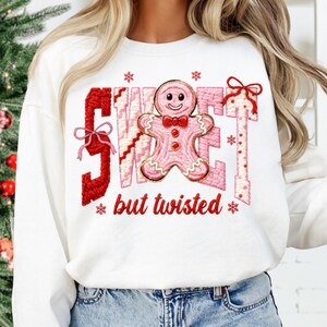 May include: White sweatshirt with the words "SWEET" and "but twisted" in red and pink embroidery. A pink gingerbread man with a red bow tie is in the center. Red bows and snowflakes are also embroidered on the sweatshirt.