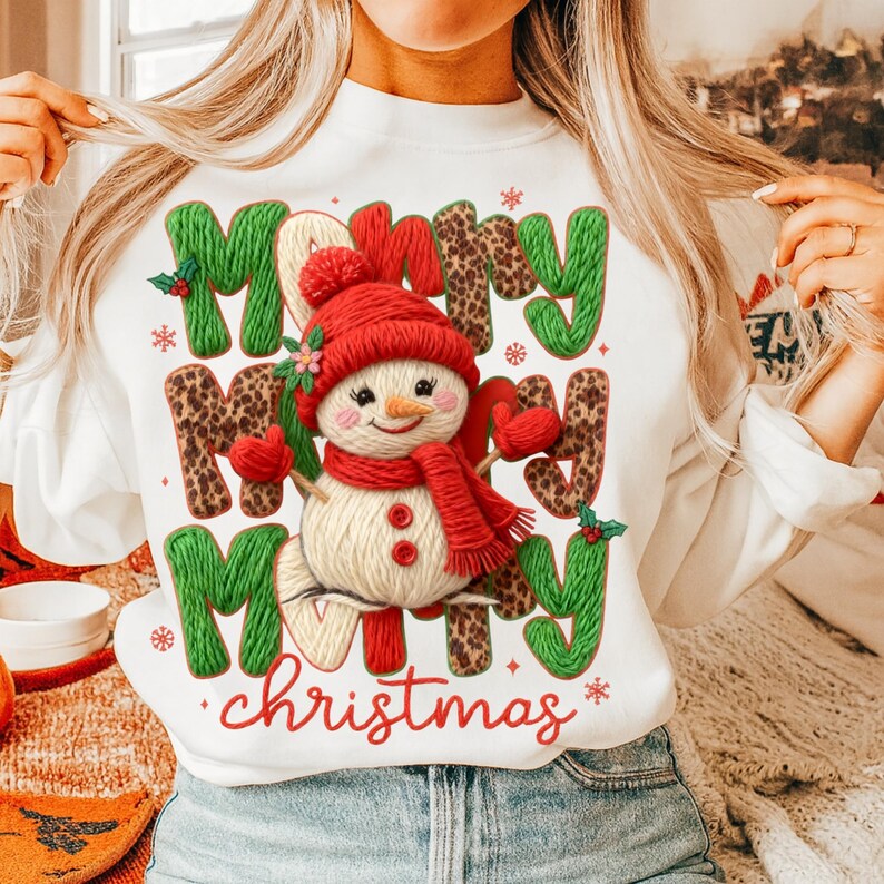 May include: White sweatshirt with a festive design featuring a snowman wearing a red hat and scarf. The words "Merry Christmas" are displayed in green, leopard print, and red lettering, with snowflakes.