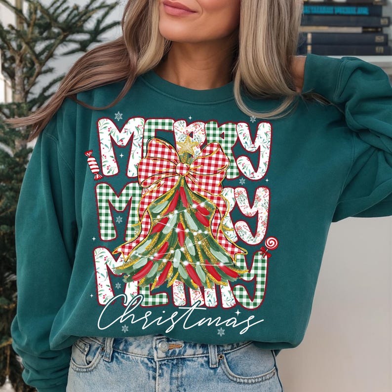 May include: Teal green sweatshirt with a festive Christmas tree design. The words "MERRY MERRY MERRY Christmas" are printed on the front in a mix of plaid and white lettering. The tree is decorated with lights and a bow.
