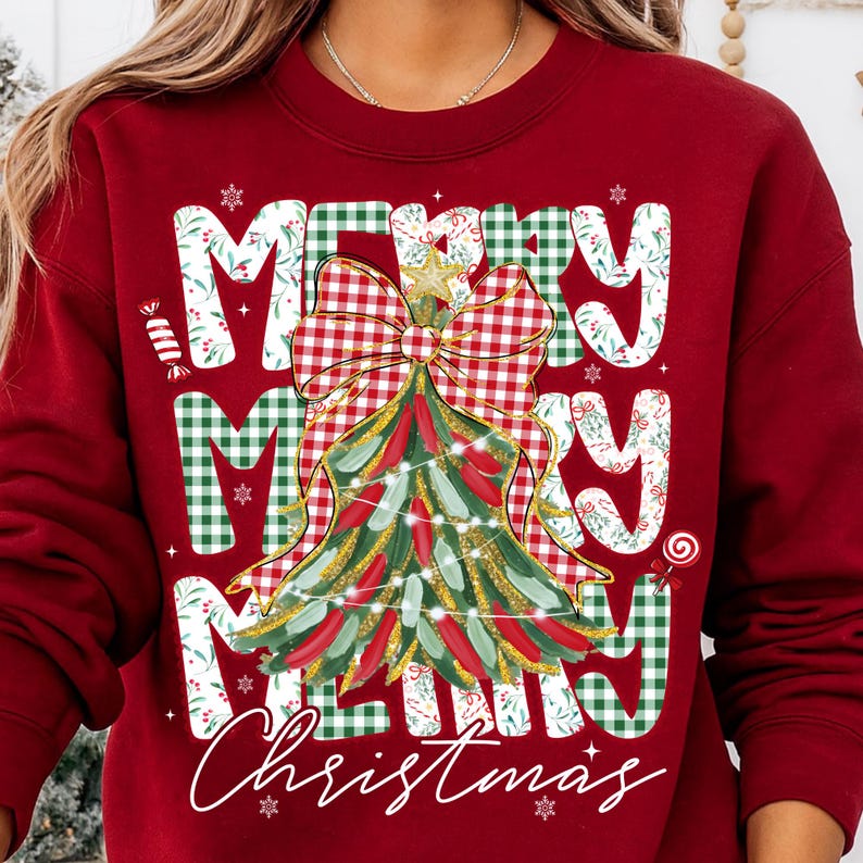 May include: A red sweatshirt with a Christmas tree design. The tree is decorated with red and green accents, a gold star, and a red and white checkered bow. The words "MERRY CHRISTMAS" are printed on the front.