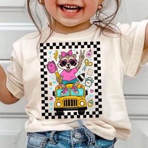 May include: A cream-colored t-shirt featuring a cartoon raccoon wearing sunglasses and a pink bow, holding a pencil and making a peace sign. The raccoon is riding a yellow school bus, surrounded by school-themed graphics.