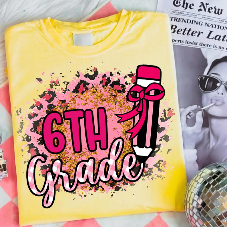 May include: Yellow t-shirt with a pink and black leopard print design. The shirt features the text "6TH Grade" in pink and white, along with a pencil graphic with a pink bow. A fun back-to-school tee.