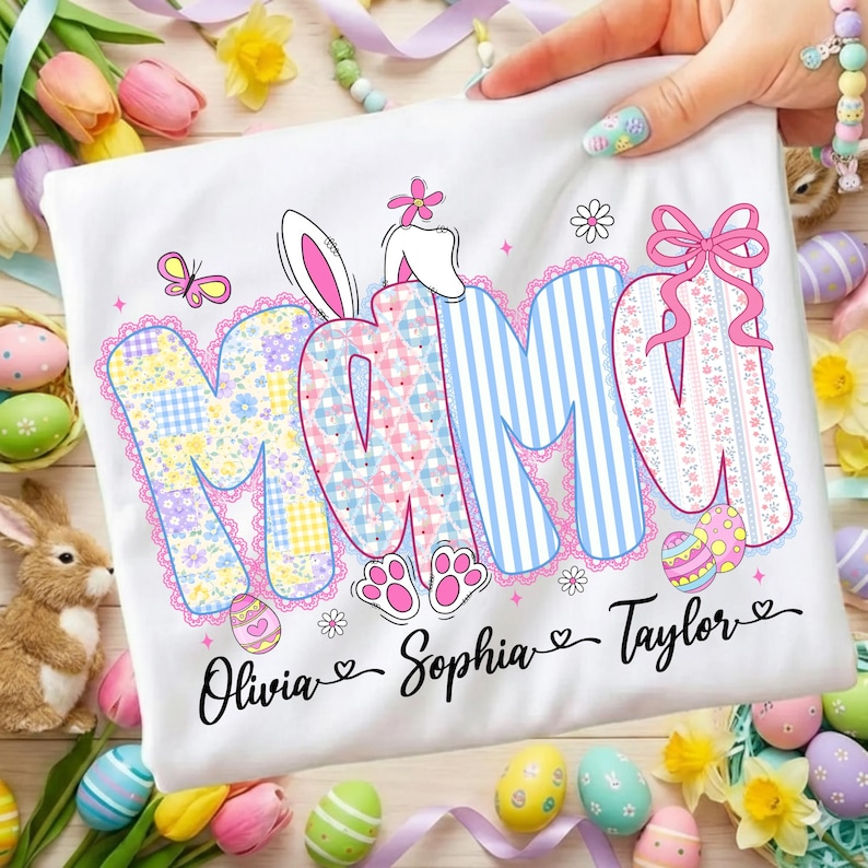 May include: White t-shirt with the word "MOM" in colorful, patterned letters, featuring a bunny ear design. The names "Olivia", "Sophia", and "Taylor" are written below. Easter-themed with eggs and flowers.