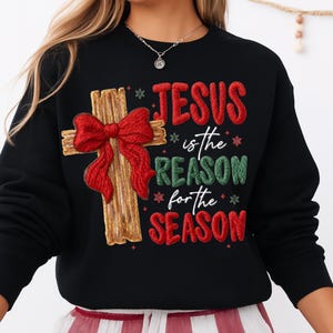 May include: Black sweatshirt with the text "JESUS is the REASON for the SEASON." The design includes a wooden cross with a red bow. The text and bow have a textured, stitched appearance, with snowflakes.